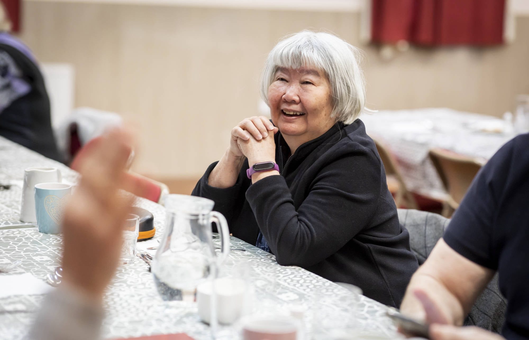 An older woman smiling while sitting at a table