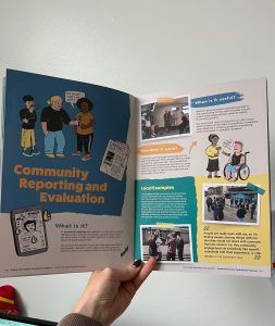 A person holds open a page of the Greater Manchester Participation Playbook featuring a section titled &ldquo;Community Reporting and Evaluation&rdquo;. The spread includes illustrated characters, explanatory text, photographs of community reporting activities, and examples from The Elephants Trail. The pages explain what community reporting is, how it works, and when it can be useful for gathering and sharing lived experience.